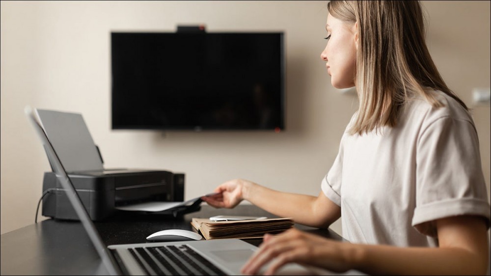 Someone using their laptop and printer in a room with a large television.