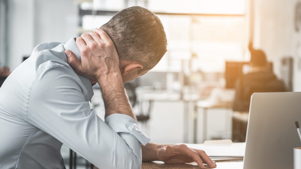 Man holding sore neck while using notebook computer.